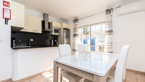 Une cuisine moderne avec des meubles blancs, un réfrigérateur en acier inoxydable et un four à micro-ondes. On y trouve une table à manger avec des chaises blanches.