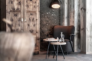 A room with a wooden wardrobe, a round table with a book and a glass, a black chair, and a wall with a textured pattern.