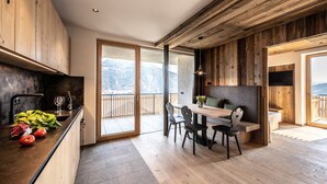 Eine moderne Küche mit Holzschränken, einem Essbereich mit einer Bank und Blick auf Berge durch große Schiebetüren.