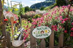 Un letrero de jardín con motivos naturales, rodeado por una valla de madera y diversas plantas con flores.