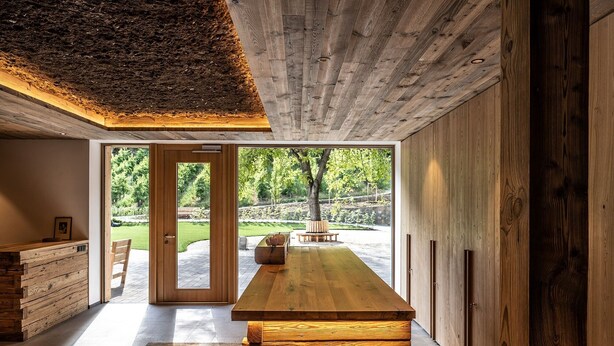 Ein modernes Interieur mit einer Holzbank, einer Tür, die zu einem Außenbereich führt, und Blick auf einen Garten.
