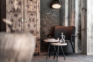 Une pièce avec une armoire en bois, une table ronde sur laquelle se trouvent un livre et un verre, une chaise noire et un mur orné d’un motif texturé.
