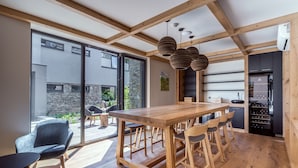 A modern kitchen with a wooden table and bar stools, large windows, and a stone wall. - Vista Resort Prague (Prague)