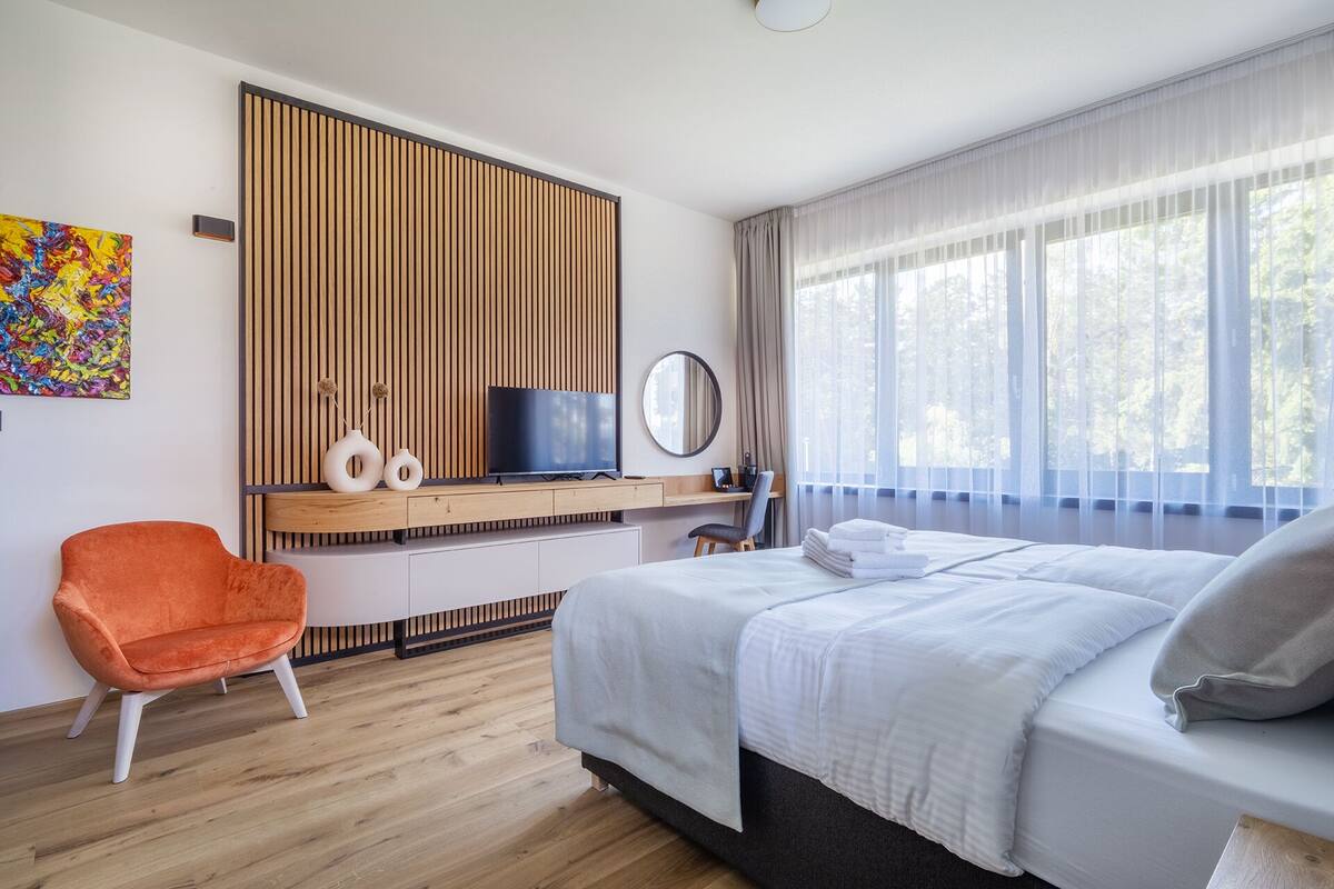 Moderni hotellihuone, jossa on sänky, työpöytä, jossa on televisio, tuoli ja suuri ikkuna, jossa on verhot.