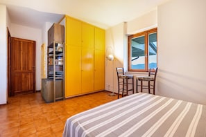 A bedroom with a bed, a wooden wardrobe, a small table with chairs, and a window with a view.
