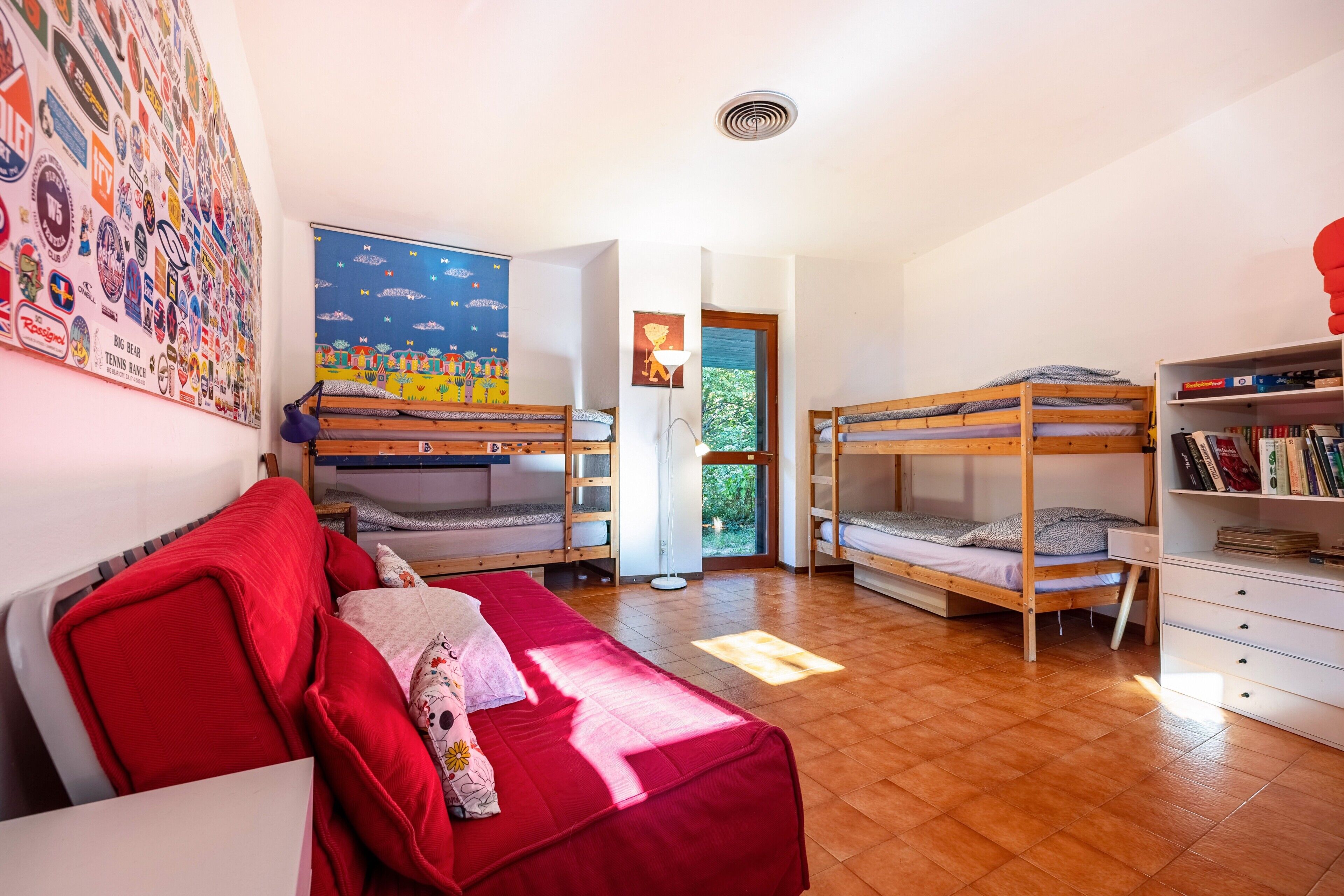 A room with bunk beds, a red sofa, a bookshelf, and a wall with various stickers.
