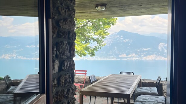 A stone wall, a wooden table, and a view of mountains and a lake.