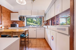 A kitchen with a wooden table, white cabinets, a window with a view of trees, and a stove.