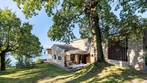 A stone building with a patio, surrounded by trees and a clear sky.