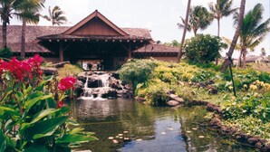 A resort with a waterfall, tropical plants, and a thatched-roof building.