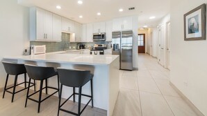 Une cuisine moderne avec des meubles blancs, des appareils en acier inoxydable et un grand îlot central doté de tabourets.