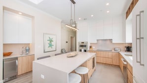 Een moderne keuken met een centraal eiland, houten kastjes en roestvrijstalen apparatuur, verlicht door een hanglamp.