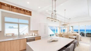Een moderne keuken met een groot eiland, witte kasten en uitzicht op de oceaan.