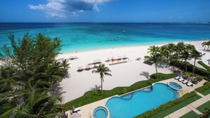 Een resort met een groot zwembad, een strand met parasols en palmbomen.