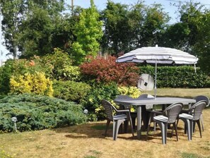 Relax in a serene outdoor space surrounded by lush greenery, complete with a round table and comfortable seating under a spacious umbrella.
