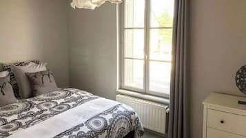 Une chambre avec une grande fenêtre, un lit avec une literie à motifs, une table de chevet et un luminaire suspendu.