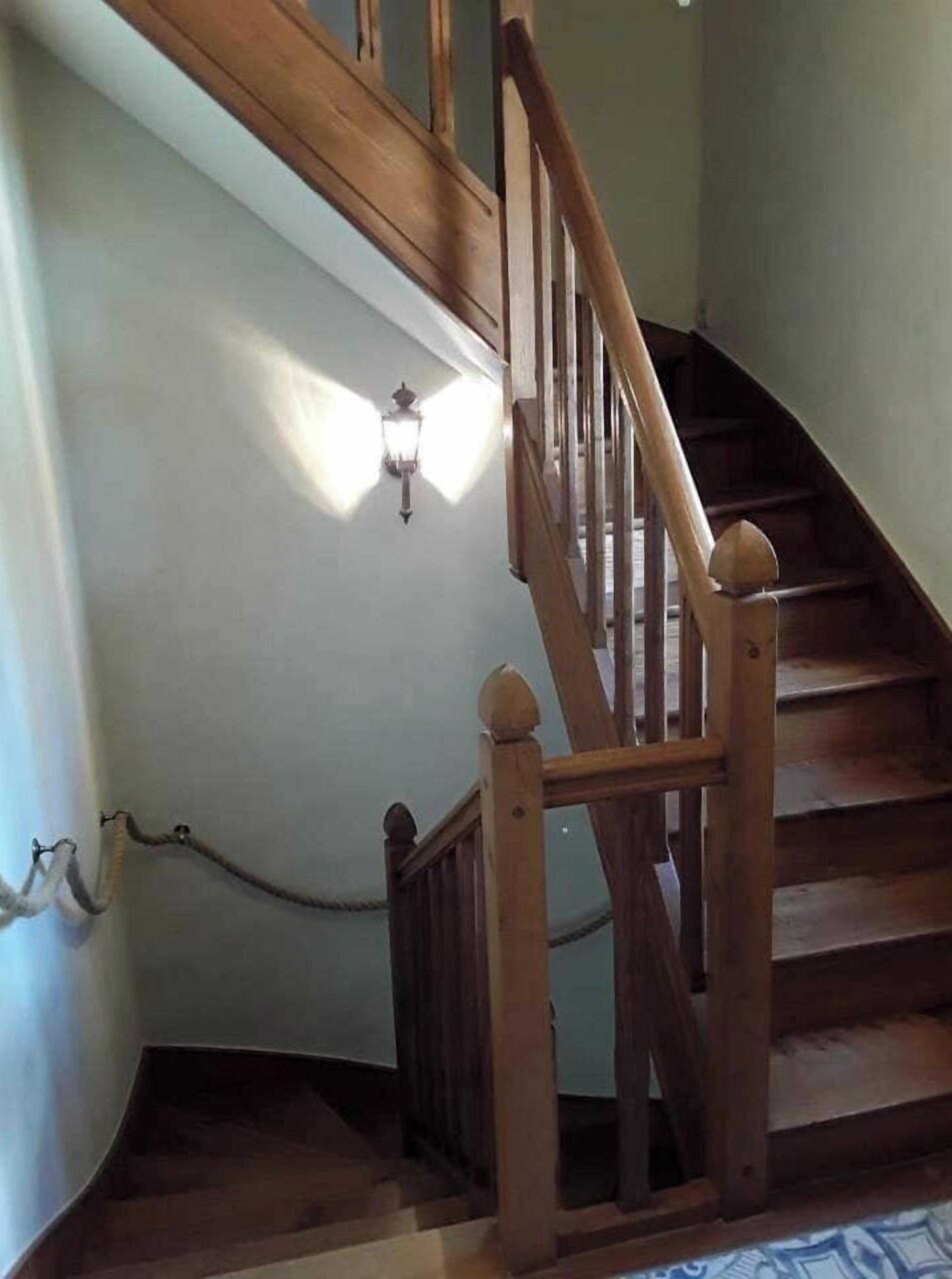 Un escalier en bois, doté d’une rampe et d’un luminaire fixé au mur.