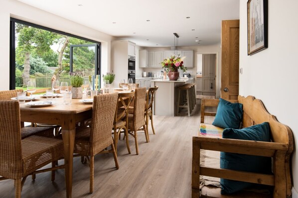 A modern kitchen with white cabinets, a central island, and a dining area with wicker furniture.