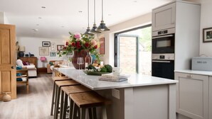 A modern kitchen with a central island, wooden stools, a large window, and a built-in oven.