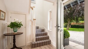 A staircase with striped carpet leading to a door, a small table with a vase of flowers, and a view of a garden outside.