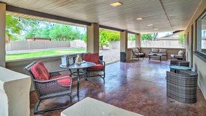 A covered patio area with outdoor furniture, including wicker chairs and a table, and a view of a landscaped yard.