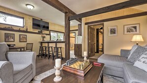 Un salon chaleureux avec un jeu d’échecs, deux canapés gris, une table basse en bois et un téléviseur en arrière-plan.