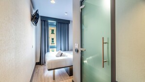 A hotel room with a bed, a glass door, and a view of the outside.