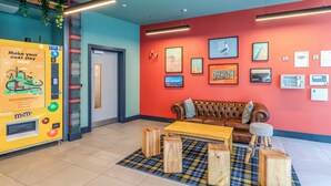 A hotel lobby with a red wall, a brown leather sofa, a wooden coffee table, and a plaid rug.