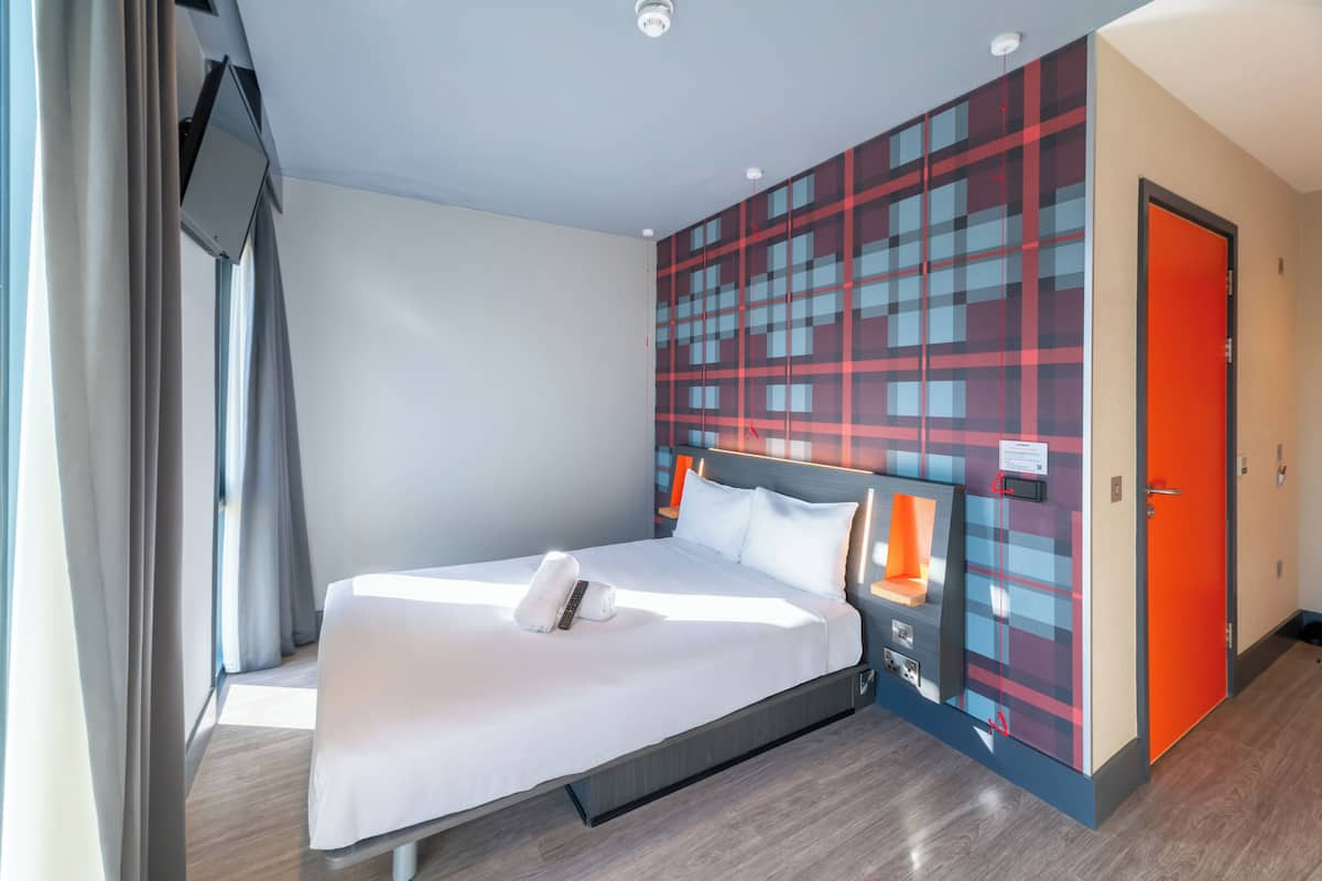 Ein modernes Hotelzimmer mit einem großen Bett, einer Wand mit rotem und blauem Muster und einer leuchtend orangefarbenen Tür.