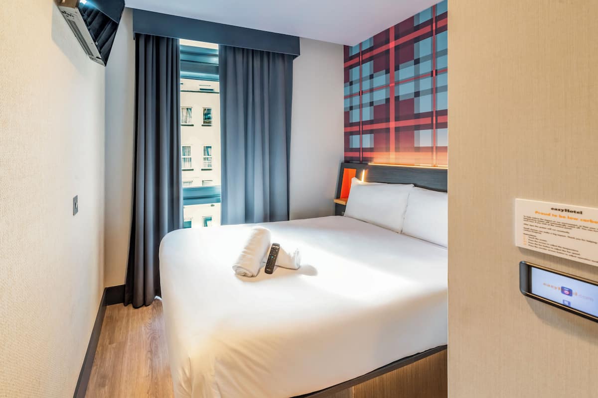 Ein Hotelzimmer mit Bett, Vorhängen, einer Wand-Klimaanlage und einem digitalen Bildschirm.