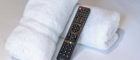 A remote control and two rolled-up towels on a white surface.