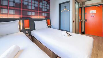 Two single beds with white linens, a red door, and a wall with a geometric pattern.