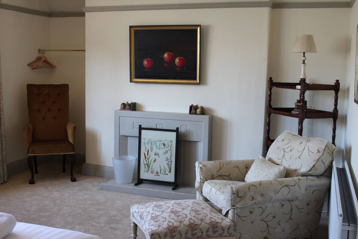 A room with a fireplace, a chair, a sofa, and a painting on the wall.