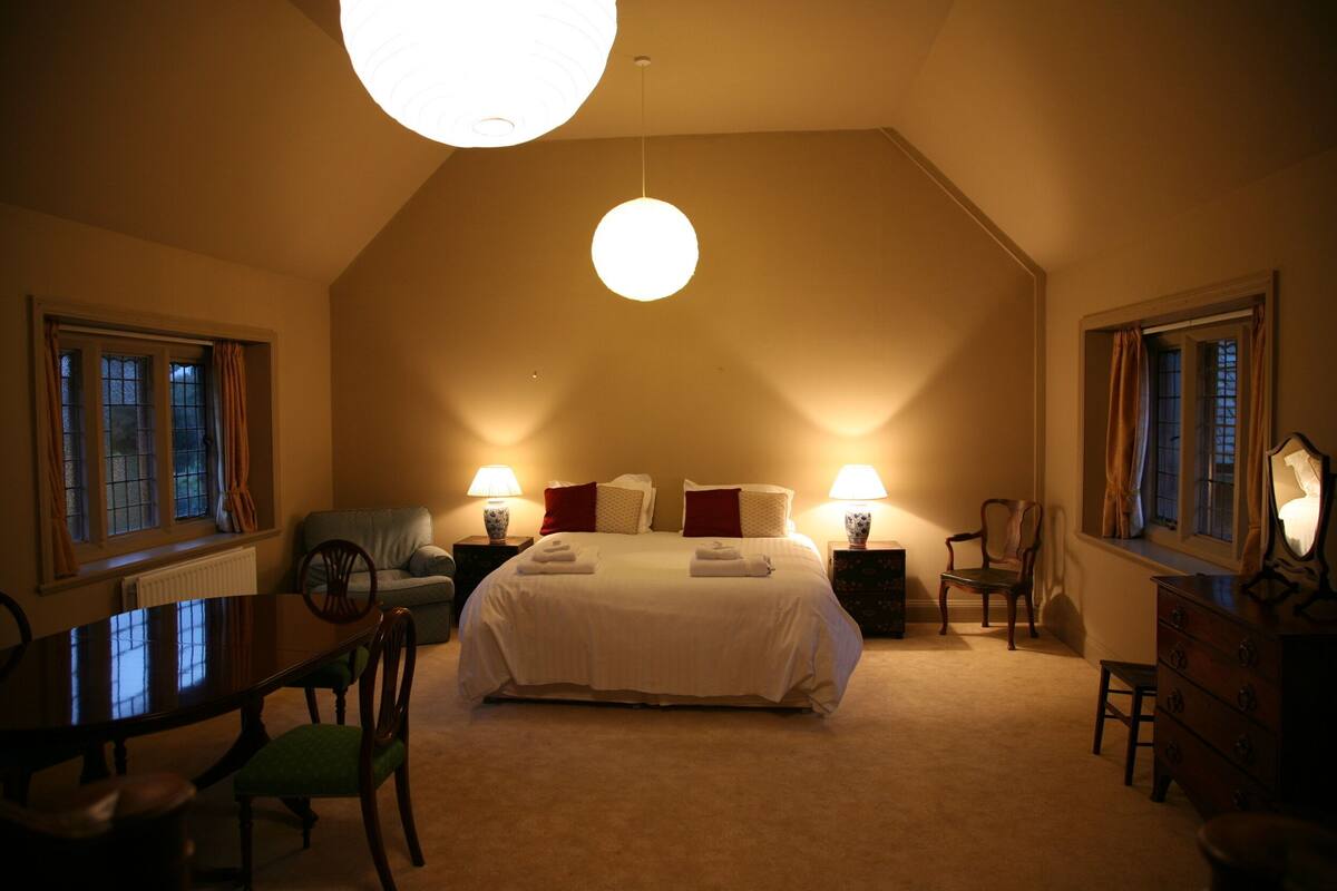 A bedroom with a large bed, two bedside tables with lamps, a desk, and a chair.