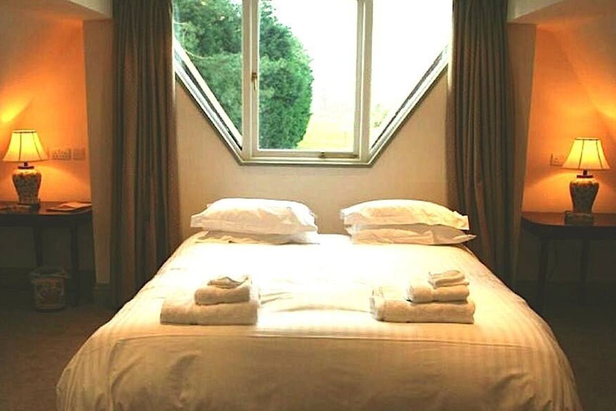 A neatly made bed with pillows and towels, two bedside tables with lamps, and a window with curtains.