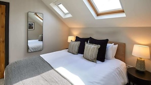 Une chambre avec un grand lit, deux lampes de chevet, un miroir et des fenêtres de toit.