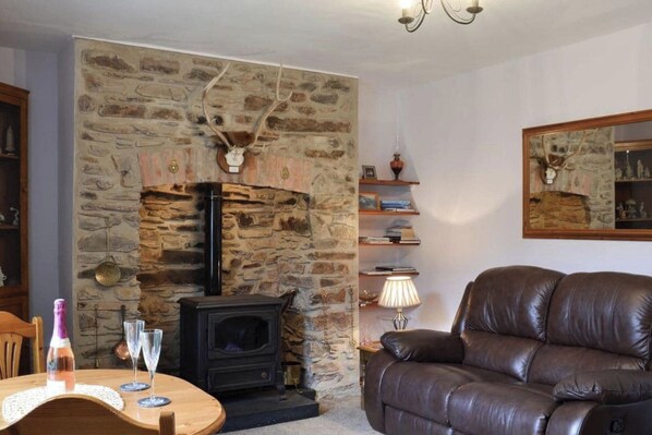 A cozy living room with a stone fireplace, a leather sofa, and a small table with a bottle and glass.