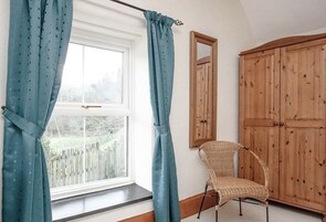Um quarto com uma janela grande, uma cadeira de vime e armários de madeira.