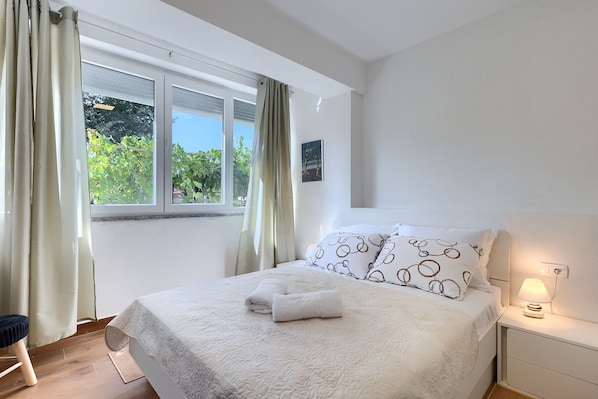 A bedroom with a bed, a nightstand, a lamp, and a window with curtains.