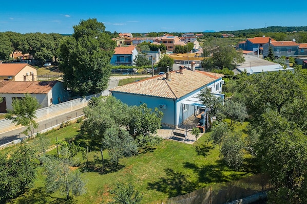 A residential area with houses, a blue building with a tiled roof, and surrounding greenery.