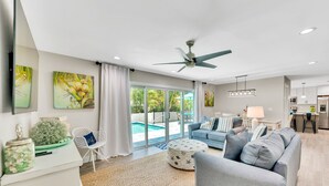 A spacious living area with a pool view, a ceiling fan, and a modern kitchen in the background. - Updated Home with Outdoor Dining and heated Pool! 2 Minutes to Beach! - Native S (Holmes Beach)