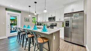 A modern kitchen with white cabinets, stainless steel appliances, and a central island with bar stools. - Updated Home with Outdoor Dining and heated Pool! 2 Minutes to Beach! - Native S (Holmes Beach)