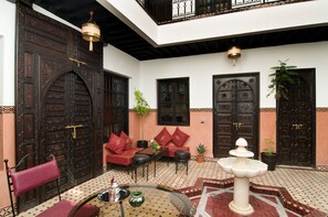 A courtyard with ornate wooden doors, a seating area with red cushions, and a fountain. - Unforgettable stay in Marrakech (Marrakesh)