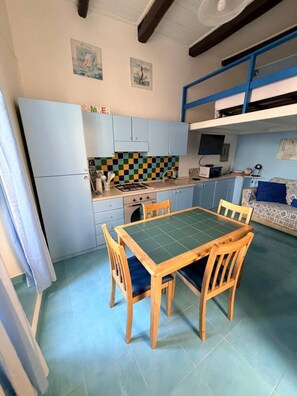 A compact kitchen with a dining table and chairs, a built-in oven, and a checkered backsplash. - Duplex Studio Casetta San Giovanni (Pizzo)