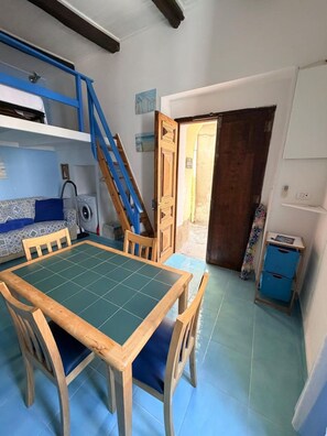 A compact room with a dining table, chairs, a bunk bed, a washing machine, and a small cabinet. - Duplex Studio Casetta San Giovanni (Pizzo)