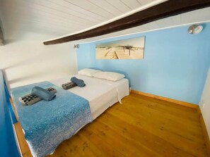 A small, single-bed room with a wooden floor, a blue wall, and a beach-themed picture. - Duplex Studio Casetta San Giovanni (Pizzo)
