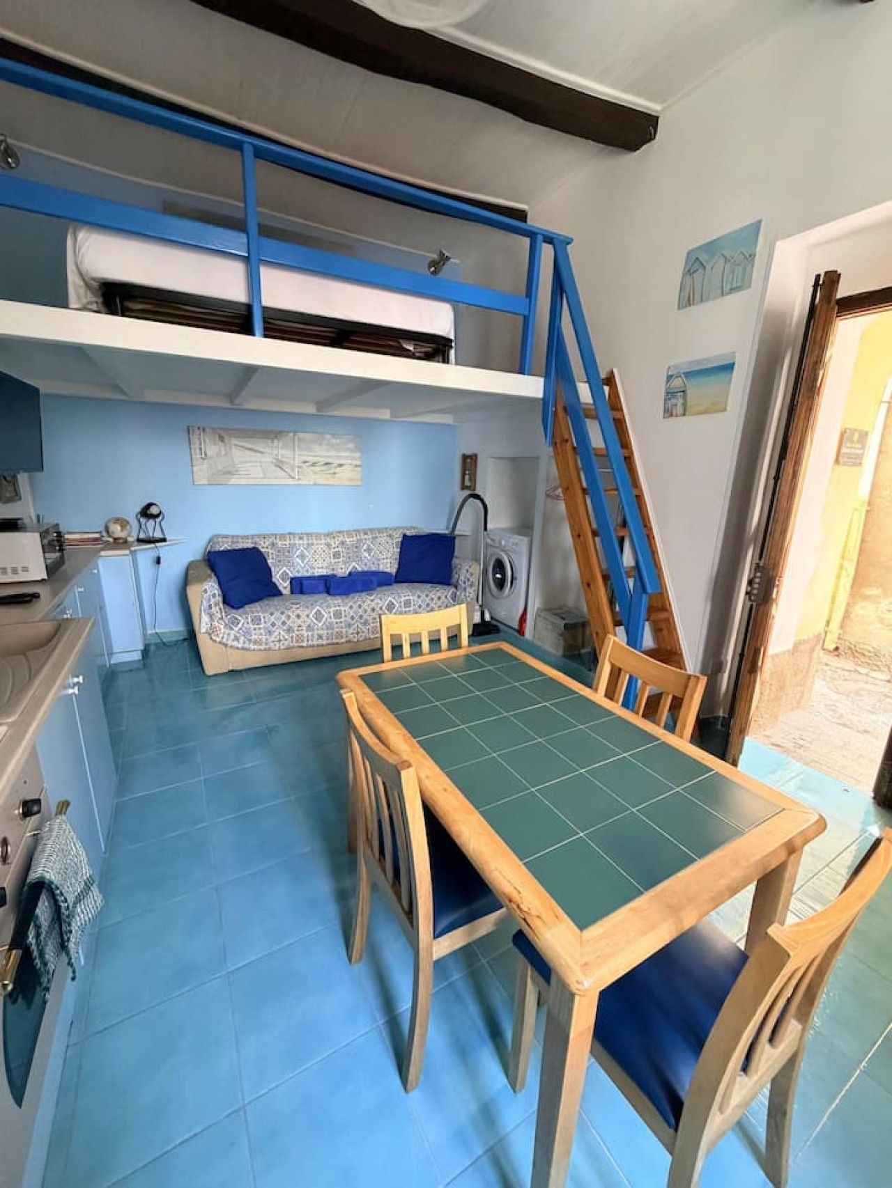 A compact living space with a bunk bed, a dining table with chairs, a washing machine, and a small kitchenette.