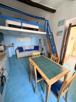 A compact living space with a bunk bed, a dining table with chairs, a washing machine, and a small kitchenette. - Duplex Studio Casetta San Giovanni (Pizzo)