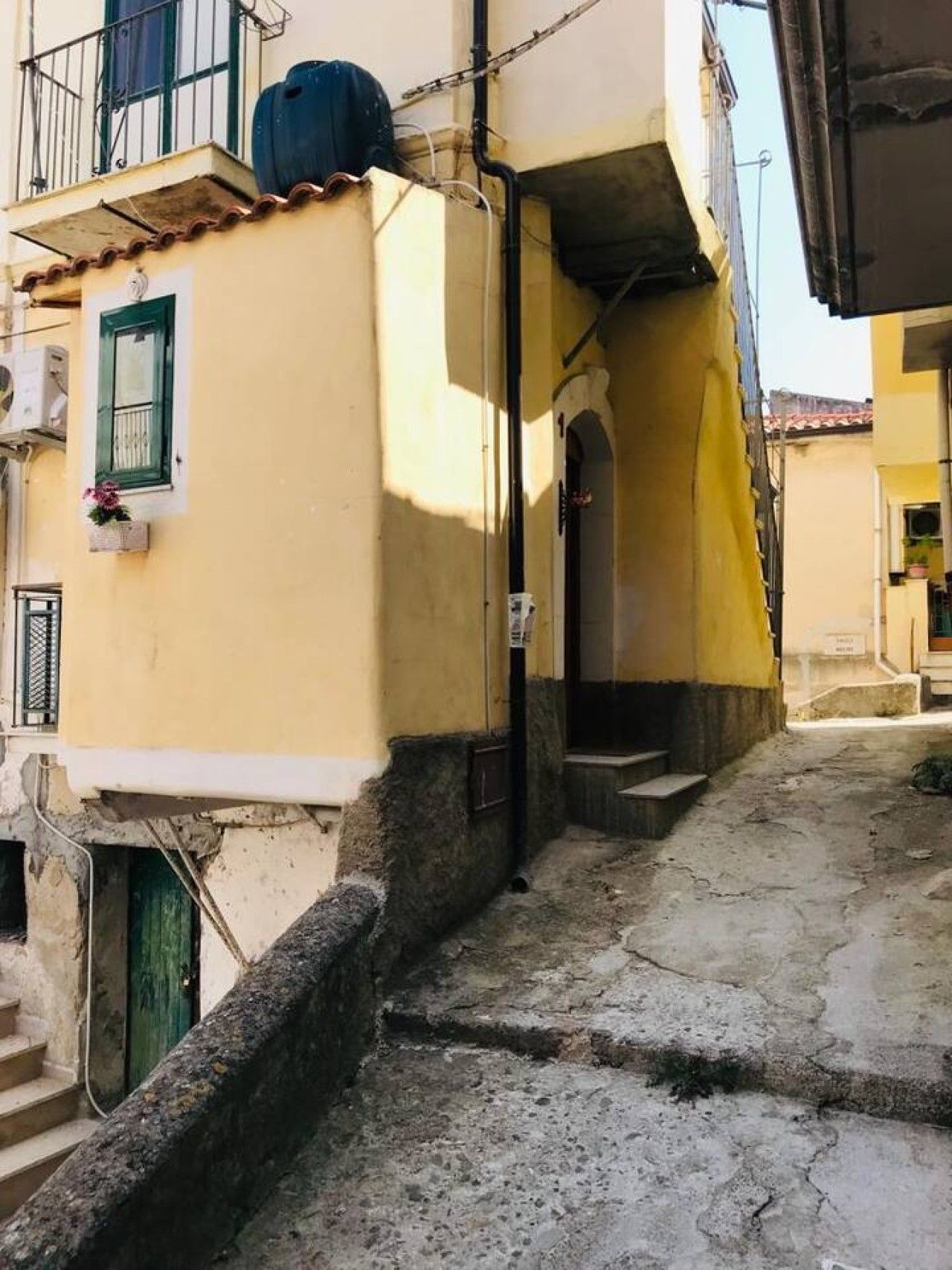 A narrow alleyway with a building featuring a small balcony and a door.
