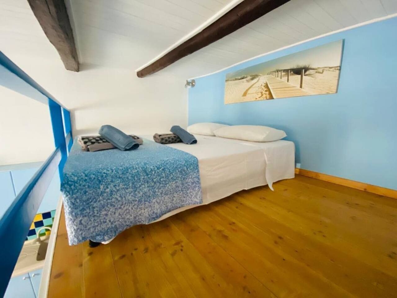 A room with a bed, a blue wall, and a wooden floor.